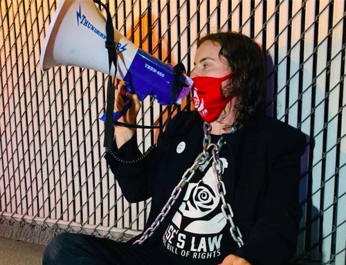 Eva Hamer chained to and seated against a wall speaking into a megaphone